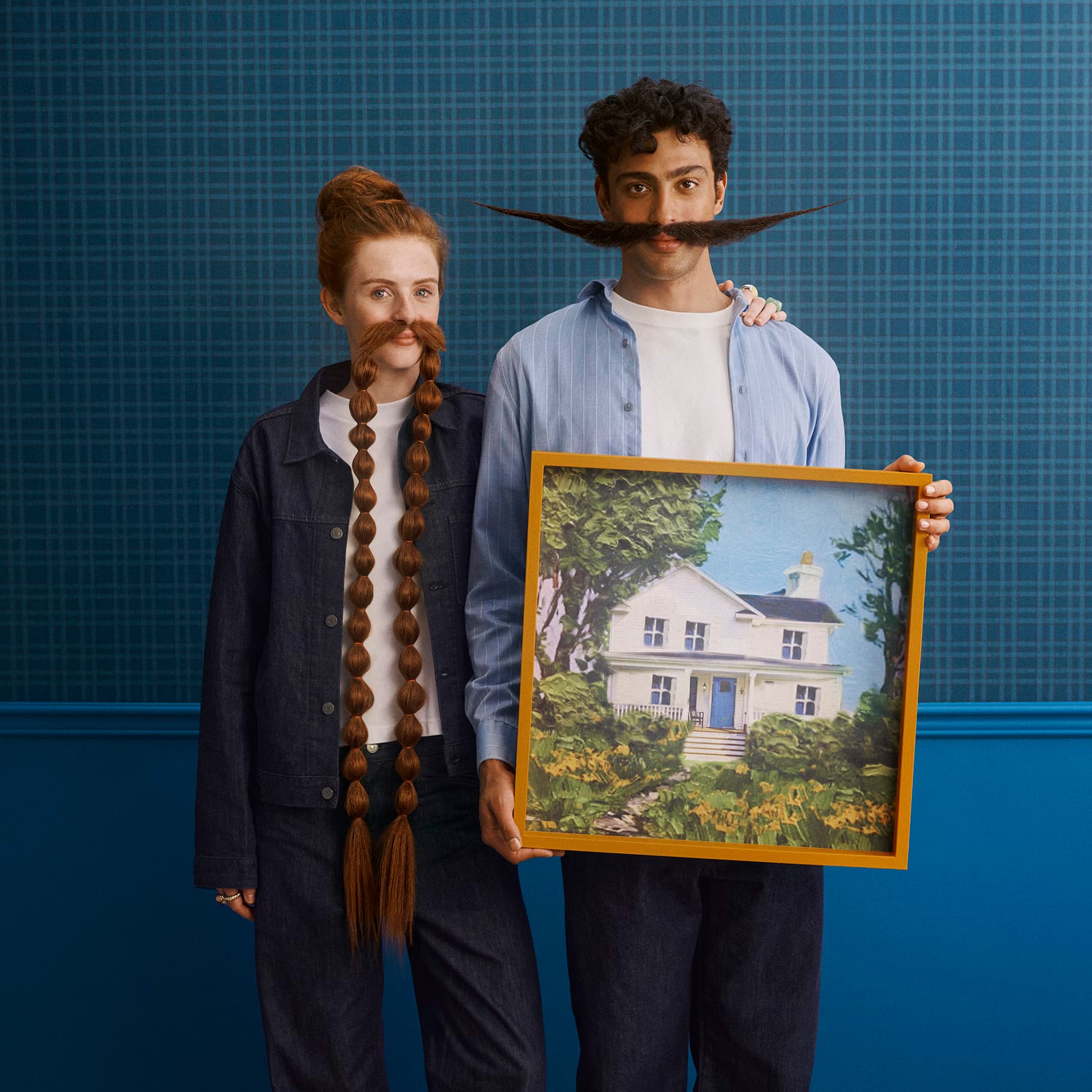 A woman with a long braided moustache and a man with a sweeping moustache holding a painting of a white house