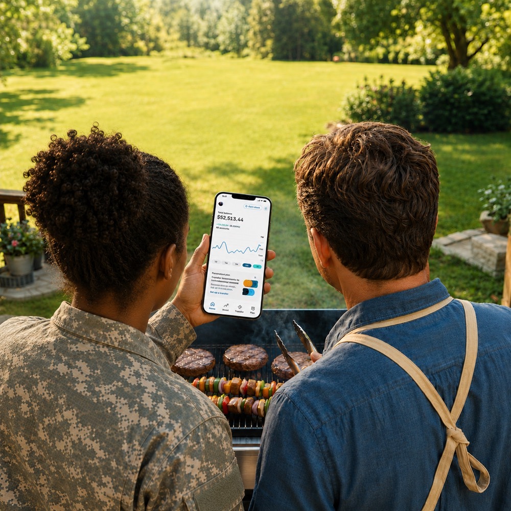 Two service members at a backyard grill look at the Stash app on a phone showing a $52,513.44 balance and an investment chart.