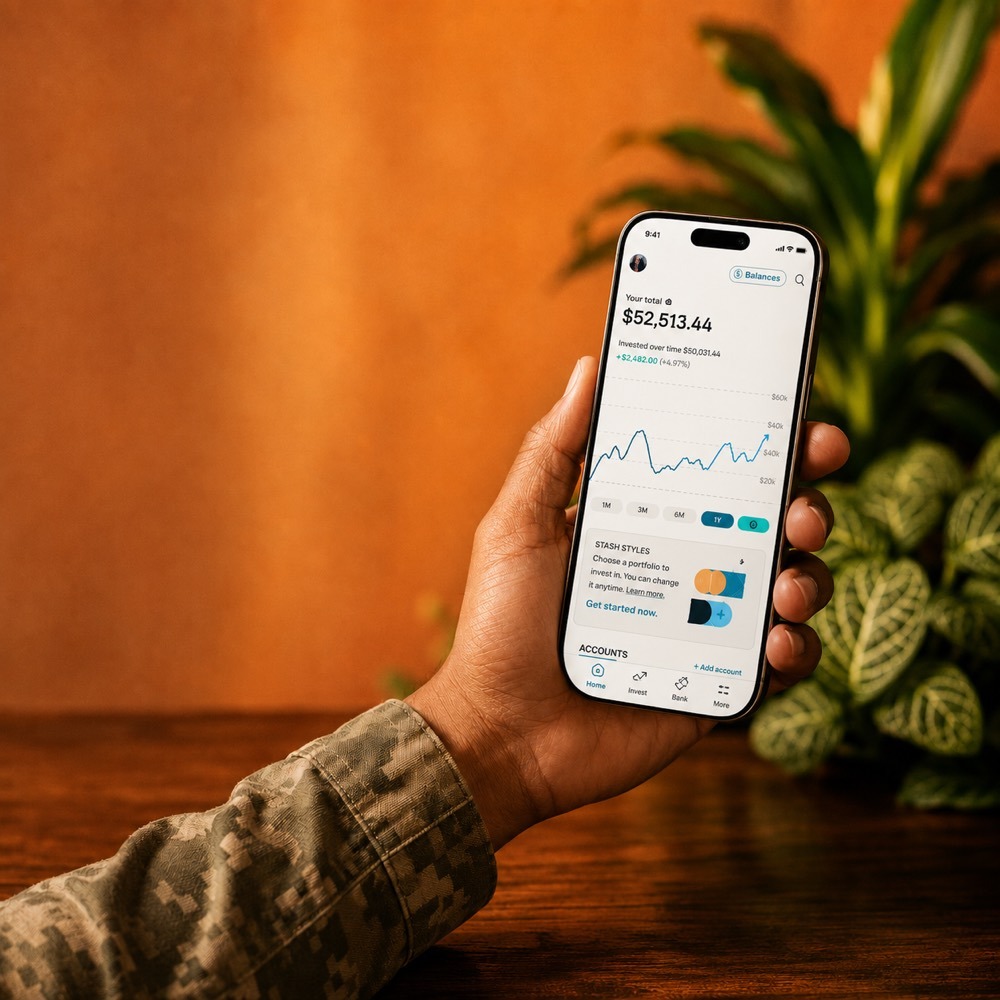 A hand in a camouflage sleeve holds a phone showing the Stash app with a $52,513.44 total and an investment chart.